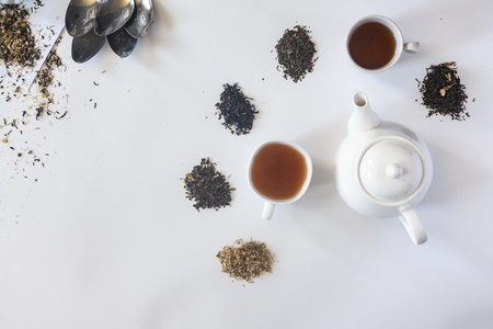 Tea set with white ceramic tea pot and other tea ingredients on the white. Flat lay view of various dried teas and teapot. View from above. Copy spaceの写真素材