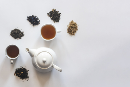 Tea set with white ceramic tea pot and other tea ingredients on the white. Flat lay view of various dried teas and teapot. View from above. Copy spaceの写真素材