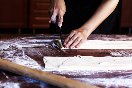 Young house wife preparing the homemade pasta at kitchen. Woman cutting long dough stripe for cooking pasta. Homemade food preparation concept.の写真素材