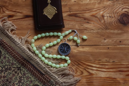 Traditional muslim prayer set bundle. Praying carpet, rosary beads, little version of the Holy Quran and qibla compass on wooden background. Copy Spaceの写真素材