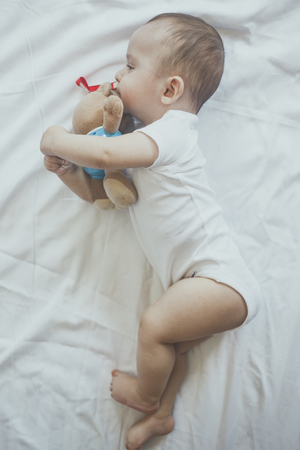 6-8-month-old baby boy lying playfully in bed. Charming 6-7 month little baby in white bodysuit. Baby boy in white bedding. Free spaceの写真素材