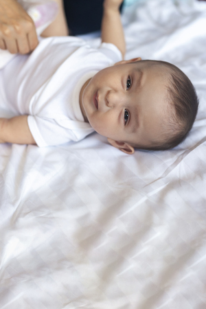 Angry 6 months old baby in bed. Little baby boy feeling uncomfortable and unhappy. Sad baby boy looking at camera. Free spaceの写真素材