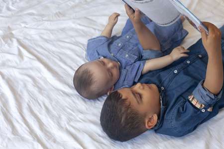 Two little brothers reading a book. Infant kids lying on the bed and read the tale before sleeping. Reading a short story for Kids. Middle eastern children on their bed. Copy spaceの写真素材