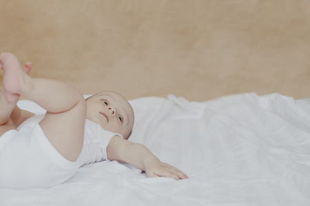 6-8-month-old baby boy lying playfully in bed. Charming 6-7 month little baby in white bodysuit. Baby boy in white bedding. Free spaceの写真素材