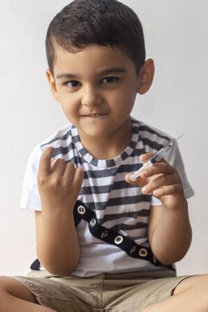 A little bad boy holding syringe and calling somone with his finger. A child having fun at hospital.の写真素材