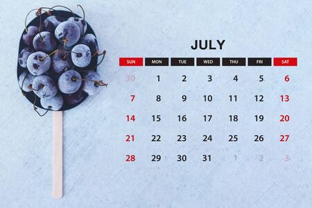 july calendar. Stack of frozen sweet cherries with July month calendar. Summer food background.の写真素材
