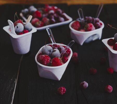 Homemade fresh yogurt. Healthy sweet dessert on dark rustic wooden background. Frozen fruits. Copy spaceの写真素材