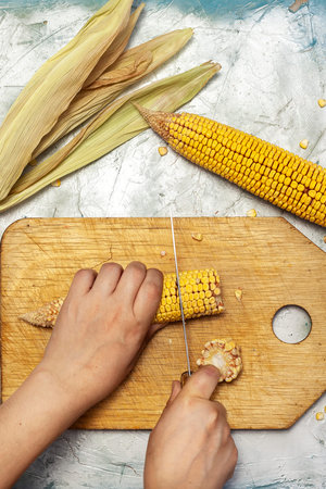 Woman hand cutting corn on cutting board. Sweet corns on desk.