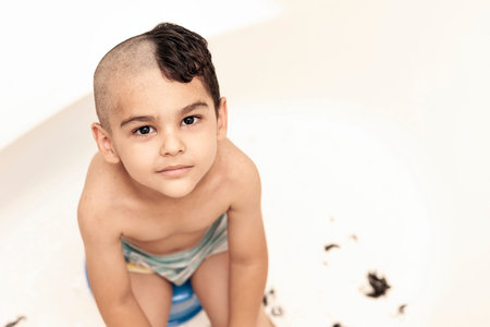 Portrait of a little middle eastern boy at the bathroom. 6-year-old pretty kid with half-cut hair at...