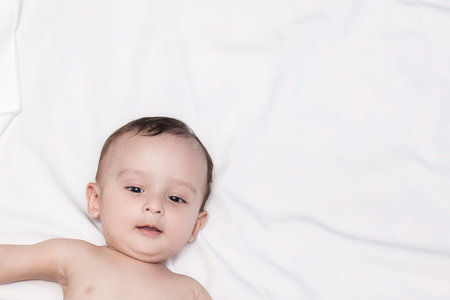 Cute 9 months old naked baby boy lying at his bed