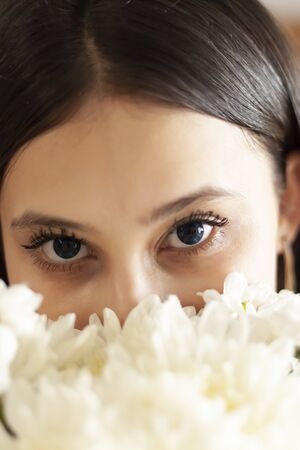 Attractive middle-eastern girl with beautiful eyes looking into the camera from behind flowers bouquet. Close-up view of young charming female.の写真素材
