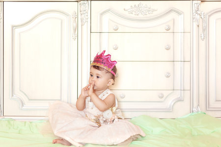 First birthday. Little cheerful baby girl with crown celebrating her first birthday party. A funny baby girl dressed as a princessの写真素材