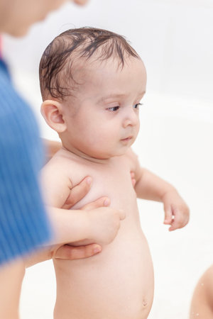 Young mother washing her baby boy's hair at bathroom. 1 year old kid taking a bath. Mother bathing...