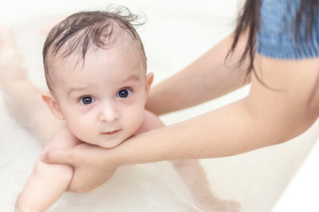 Young mother washing her baby boy's hair at bathroom. 1 year old kid taking a bath. Mother bathing her babyの写真素材