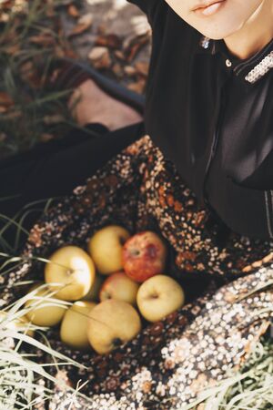 Portrait of beautiful middle-eastern woman at apple garden. Young female posing with freshly picked autumn apple fruits. Portrait of woman at nature. Eating fresh apple. Autumn portrait of Apple womanの写真素材