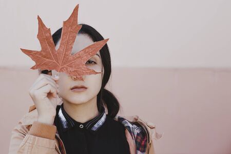 Autumn woman. Fall season concept. A portrait of pretty female with an yellow autumn leaf. Young female hiding her face with fall leaves. Autumn or fall woman. Sunny autumn weather at outdoors.の写真素材