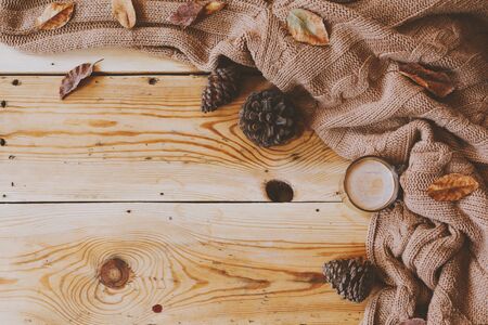 Autumn background. A cup of hot coffee, knitted scarf and pinecones on wooden table. Autumn coffee. Knitted woolen sweater, coffee and fall leaves over rustic wood board. Top view. Copy spaceの写真素材