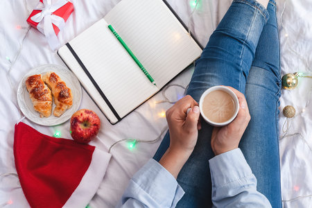 Young woman lying and having breakfast in bed. Christmas morning in a cozy bedroom decorated with...