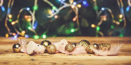 Cute Christmas toys with light pink feathers on wooden table against Christmas tree on backgroundの写真素材