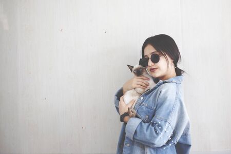 Young attractive woman hugging pussy cat in hands. Cute and glamorous girl in trendy sunglasses posing with her. Beautiful young girl holding her adorable catの写真素材