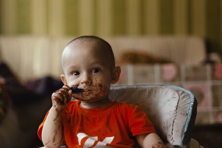 Little kid eating chocolate. Happy little Boy smeared with chocolate around his mouth. Unhealthy eating conceptの写真素材