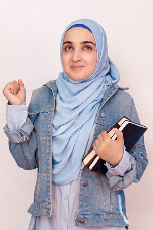 Happy Muslim businesswoman celebrating her first success in business. Attractive Muslim student holds notepads and celebrates successfully passed exams. Lovely stylish Muslim girl feels happyの写真素材