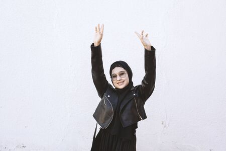 Happy Iranian girl putting hands up and dancing. Excited young female celebrating a victory. Smiling Muslim woman in traditional Islamic clothing - hijab. Birthday, New Year celebration conceptの写真素材