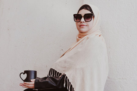 Pretty middle eastern girl in traditional Islamic clothing, drinking cup of coffee. Cute Arabian...