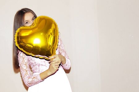young beautiful girl in white dress embracing heart shaped golden air balloon. valentines day, birthday, womens day, anniversary, holiday celebration conceptの写真素材