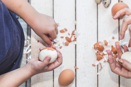 Little kid helping the mother to prepare breakfast. 6 years old child cleans the shell of the egg. A...