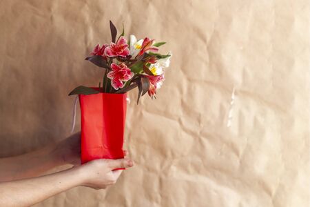 Flower shop. Giving flowers. Hands holding spring flowers bouquet against the crafty paper background. Copy space for your text, ad, or messageの写真素材
