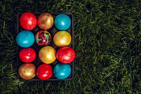 An egg carton full of colorful Easter eggs on the green grass background. View from above. Copy space for your text or adの写真素材