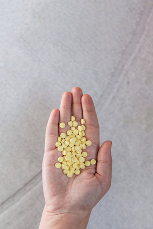 Woman holding yellow pills in hand. Top view