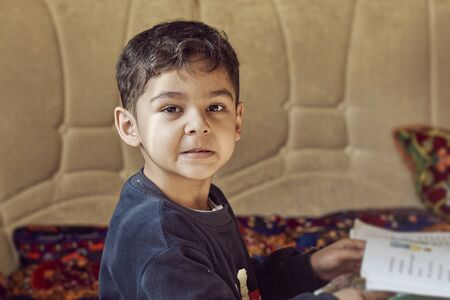 A little schoolboy doing homework. Reading book. Authentic view of a young kid in a cozy home environmentの写真素材