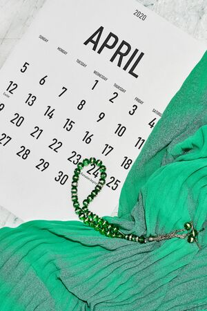 April monthly calendar on green silk textile background. Islamic Ramadan Eid festive background with Islamic praying rosary beadsの写真素材