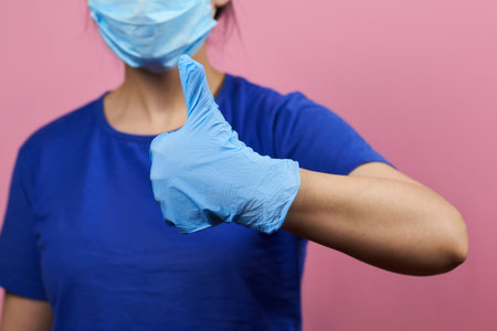Woman in medical facial mask and protective gloves showing thumbs-up.