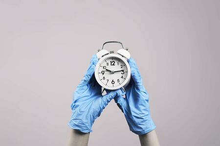 Hands in protective medical gloves holding an alarm clock.の写真素材