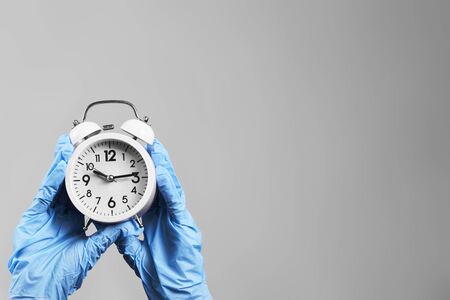 Hands in protective medical gloves holding an alarm clock.の写真素材