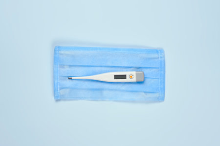 Medical face mask and thermometer on bright blue background