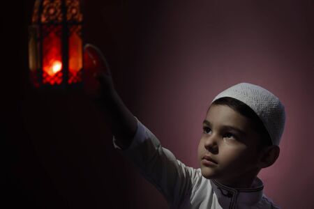 Muslim boy touching traditional Arabic lantern candle blowing in the dark. Middle-eastern boy praying. Thanking god. Ramadan, Eid-al-Adha conceptsの写真素材