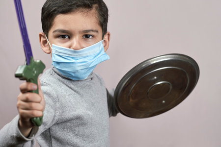 Bored boy in medical face mask plays knight cavalier. Little moddle-eastern kid in surgical masks...