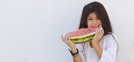 Portrait of a beautiful teen girl eating watermelon at outdoors. A little girl holding in hands big slice of sweet fresh juicy watermelon. Face expression, Feeling happy, Fun, Playful and Joyful teenの写真素材