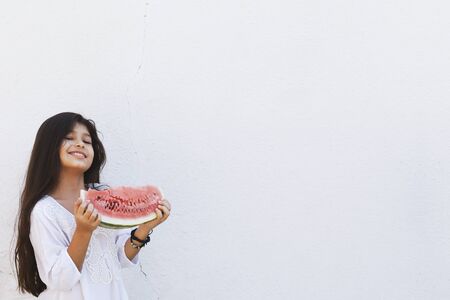 Portrait of a beautiful teen girl eating watermelon at outdoors. A little girl holding in hands big slice of sweet fresh juicy watermelon. Face expression, Feeling happy, Fun, Playful and Joyful teenの写真素材