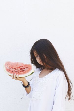 Portrait of a beautiful teen girl eating watermelon at outdoors. A little girl holding in hands big slice of sweet fresh juicy watermelon. Face expression, Feeling happy, Fun, Playful and Joyful teenの写真素材