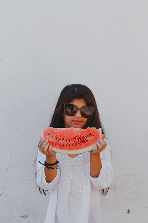 Portrait of a beautiful teen girl eating watermelon at outdoors. A little girl holding in hands big slice of sweet fresh juicy watermelon. Face expression, Feeling happy, Fun, Playful and Joyful teenの写真素材