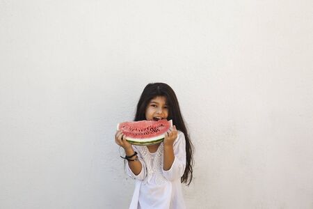 Portrait of a beautiful teen girl eating watermelon at outdoors. A little girl holding in hands big slice of sweet fresh juicy watermelon. Face expression, Feeling happy, Fun, Playful and Joyful teenの写真素材