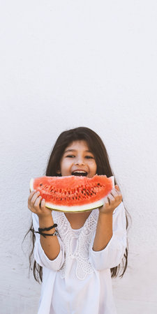 Portrait of a beautiful teen girl eating watermelon at outdoors. A little girl holding in hands big slice of sweet fresh juicy watermelon. Face expression, Feeling happy, Fun, Playful and Joyful teenの写真素材