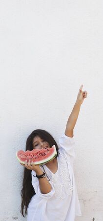 Portrait of a beautiful teen girl eating watermelon at outdoors. A little girl holding in hands big slice of sweet fresh juicy watermelon. Face expression, Feeling happy, Fun, Playful and Joyful teenの写真素材
