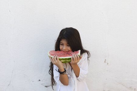Portrait of a beautiful teen girl eating watermelon at outdoors. A little girl holding in hands big slice of sweet fresh juicy watermelon. Face expression, Feeling happy, Fun, Playful and Joyful teenの写真素材