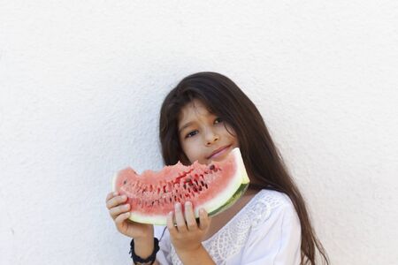 Portrait of a beautiful teen girl eating watermelon at outdoors. A little girl holding in hands big slice of sweet fresh juicy watermelon. Face expression, Feeling happy, Fun, Playful and Joyful teenの写真素材